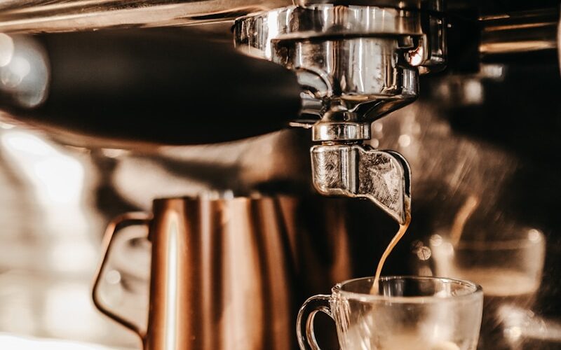 grey industrial coffee maker pouring espresso in clear glass cup